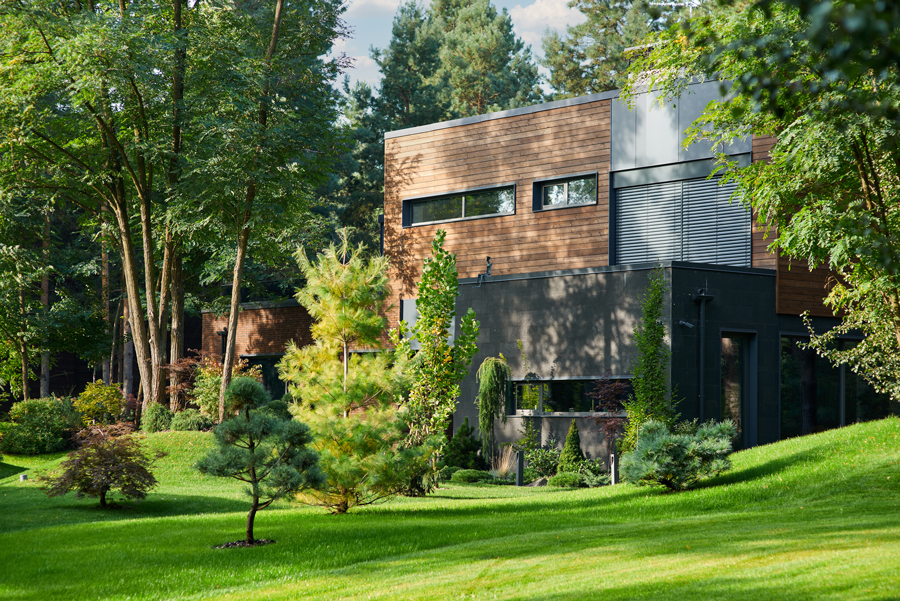 Modern house with wood accents nestled in a lush, green garden. Tall trees surround the home, creating a serene, peaceful ambiance.