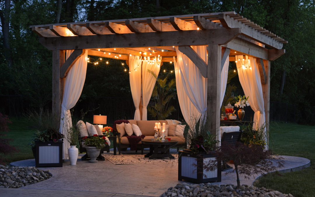 Cozy outdoor gazebo with string lights and curtains at dusk. Features a cushioned sofa, candles, and plants, creating a warm, inviting atmosphere.